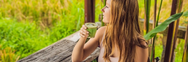 Mujer joven sosteniendo una taza de té verde con leche matcha en una vieja mesa de fondo de madera de formato largo