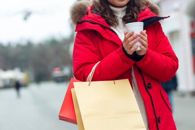 Mujer joven sosteniendo té al aire libre en la calle de invierno