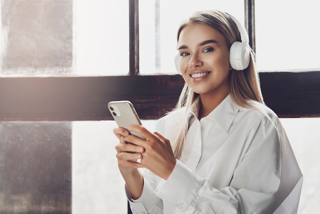 Mujer joven sosteniendo el teléfono inteligente en las manos, escuchando música en auriculares.