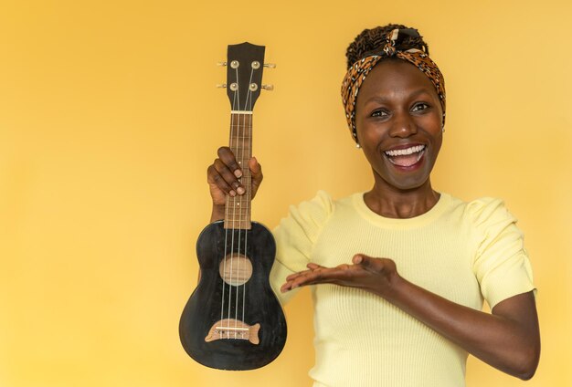 Mujer joven sosteniendo un ukelele mientras sonríe con un fondo amarillo.