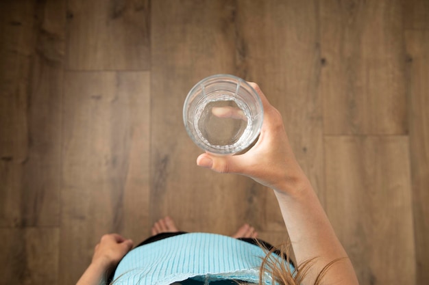 Mujer joven sosteniendo un vaso de agua mientras está de pie sobre un piso de madera Vista superior plana