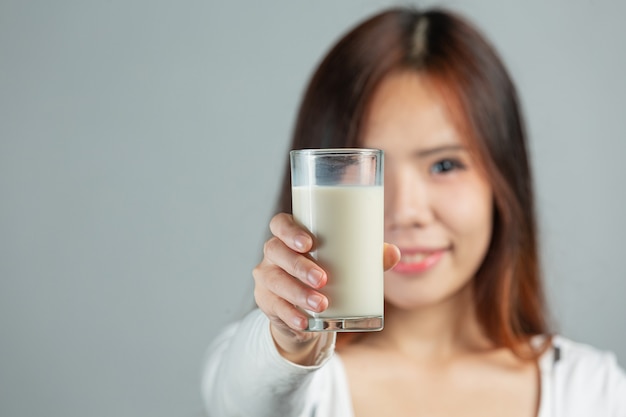 Mujer joven sosteniendo un vaso de leche sobre la superficie gris