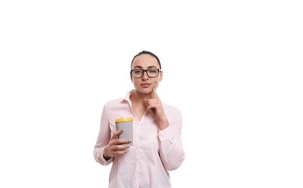 Mujer joven sosteniendo un vaso de papel reciclable de cartón con bebida caliente y posando sobre fondo blanco con espacio de copia.