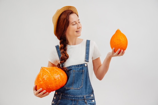 Mujer joven sostiene una cosecha de calabazas naranjas sobre un fondo blanco mientras mira uno