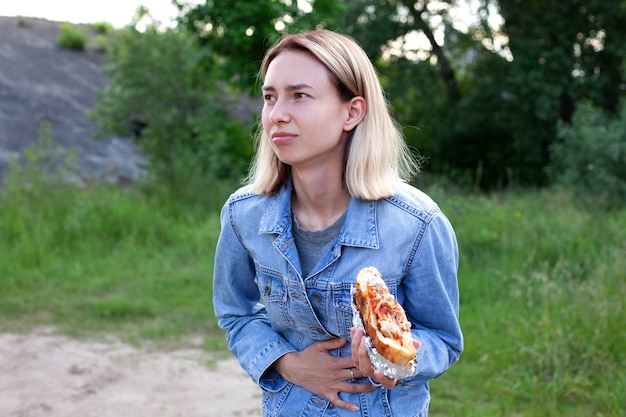 Una mujer joven sostiene una hamburguesa grande Comida no saludable comida pesada Mujer tiene dolor de estómago por hamburguesa