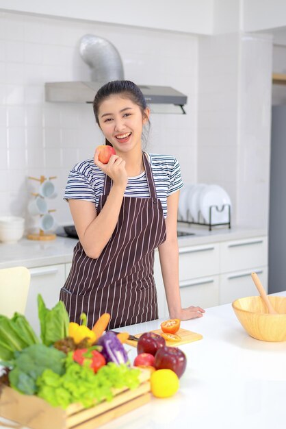 Una mujer joven sostiene una manzana roja en la cocina con un rostro alegre