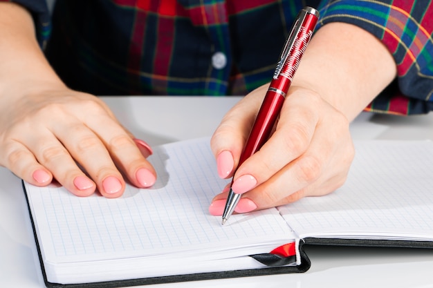 La mujer joven sostiene una pluma en su mano izquierda y escribe la nota en el cuaderno en blanco. Día internacional de zurdos