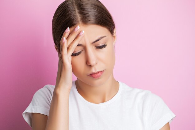 Una mujer joven sostiene su mano cerca de su cabeza y siente un fuerte dolor de cabeza