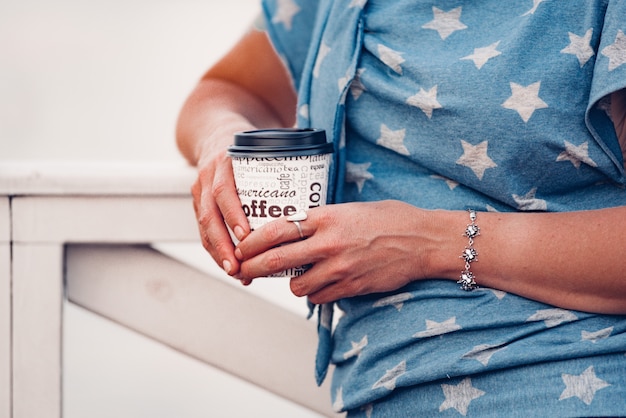 Mujer joven sostiene una taza de café desechable de papel blanco.