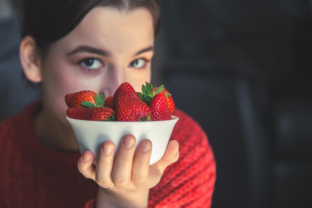 Una mujer joven sostiene un tazón de fresas en sus manos.