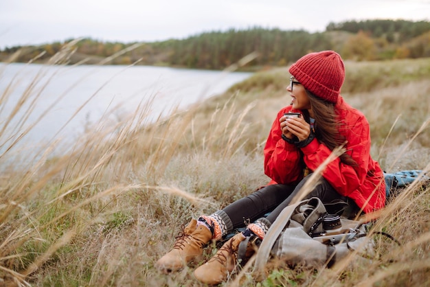 Mujer joven sostiene termo bebe té en el bosque de otoño Descanso relajación viaje estilo de vida concepto