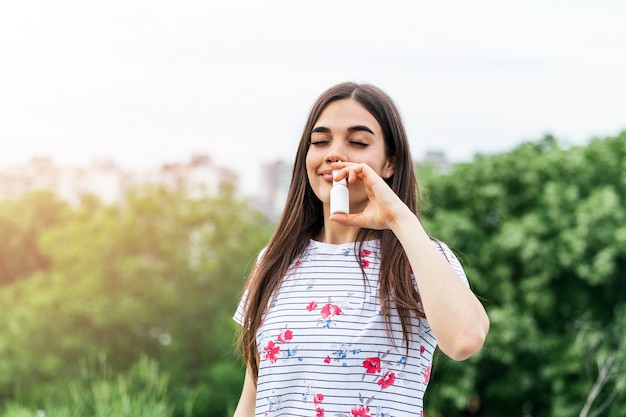 Mujer joven con spray nasal para sus alergias al polen y al pasto