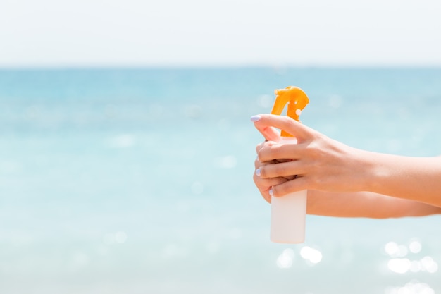 Mujer joven con spray de protección solar para el cuerpo en la playa.