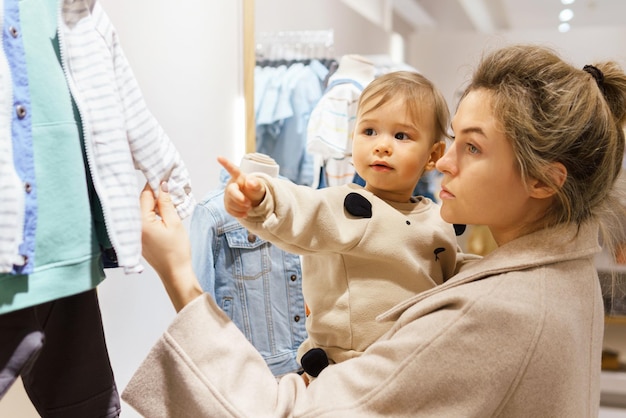 Mujer joven con su hijo eligiendo ropa en la tienda de ropa