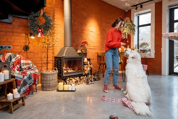 Foto mujer joven con su lindo perro blanco durante unas felices vacaciones de año nuevo cerca de la chimenea en casa