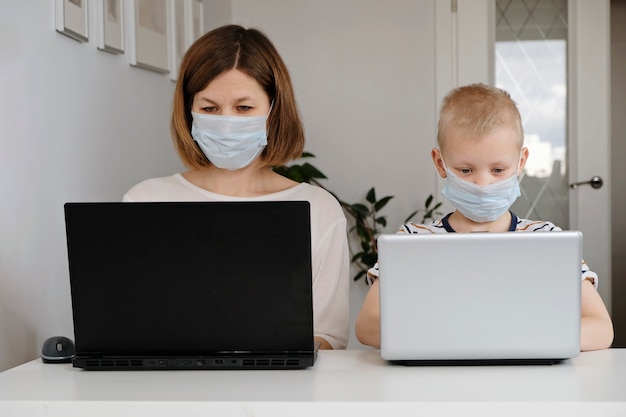 Una mujer joven y su pequeño hijo se sientan en una casa durante la cuarentena y estudian en la escuela de Internet usando una computadora.