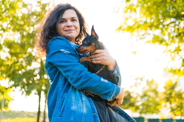 Mujer joven con su perrito al aire libre. Perro hembra pinscher miniatura negro y fuego con propietario en un parque