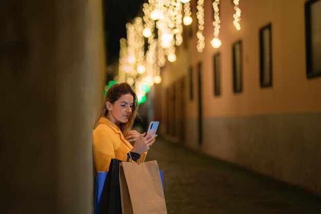 Mujer joven con su smartphone compartiendo sus compras navideñas en las redes sociales