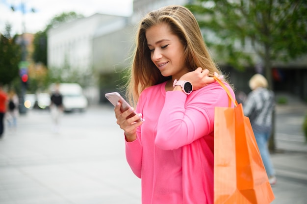 Foto mujer joven con su teléfono inteligente mientras compra en una ciudad