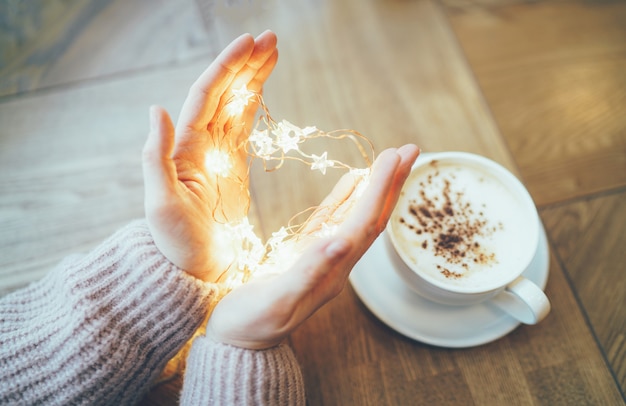 Foto mujer joven en suéter beige acogedor con corazón de guirnalda de estrellas