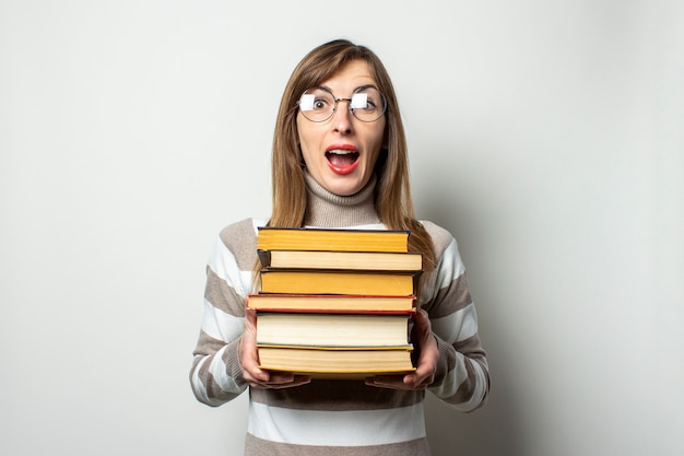 Mujer joven en un suéter y gafas sosteniendo una pila de libros