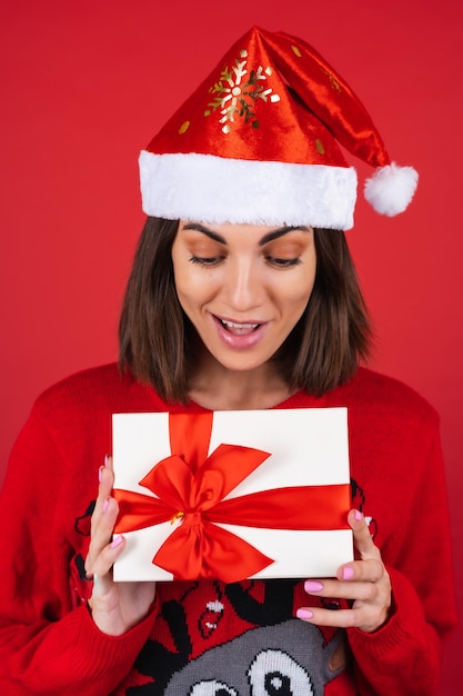 Mujer joven en un suéter de Navidad y gorro de Papá Noel con una caja de regalo