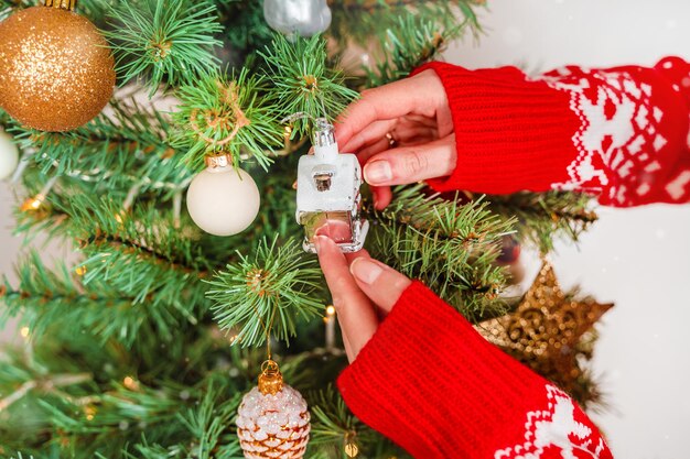 Una mujer joven con un suéter rojo cuelga juguetes de Navidad en el árbol en casa