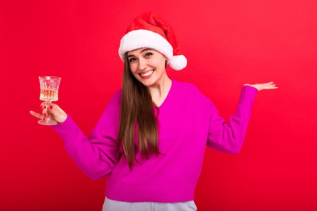 Una mujer joven con un suéter rosa con un sombrero de Santa Claus sostiene una copa de champán El concepto de celebrar la Navidad