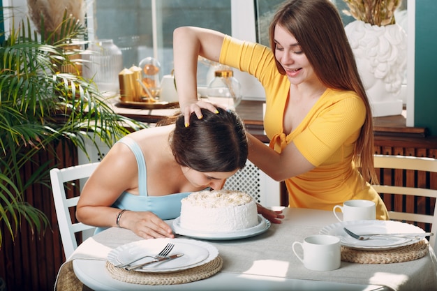 Mujer joven sumerge la cara en pastel blanco con crema. Concepto de feliz cumpleaños.