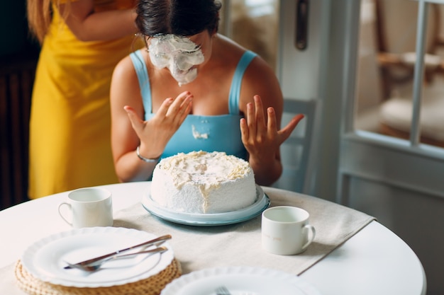 Mujer joven sumerge la cara en pastel blanco con crema. Concepto de feliz cumpleaños.