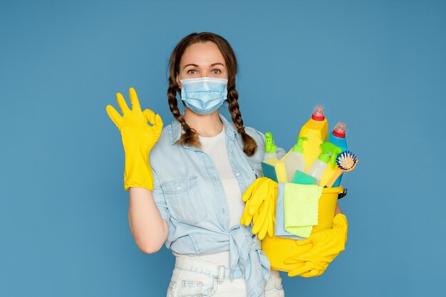 Mujer joven con suministros de limpieza en un cubo aislado en azul