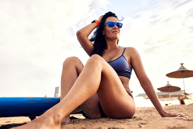 Foto mujer joven con tabla de surf sentada en la playa