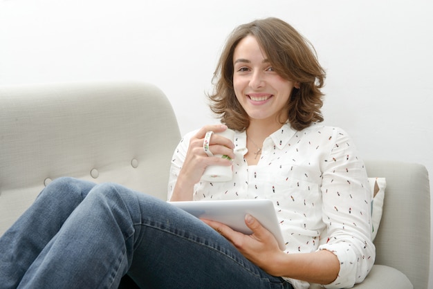 mujer joven con una tableta bebe una taza de té