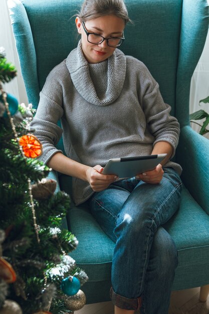 Mujer joven con tableta en el fondo de un árbol de Navidad