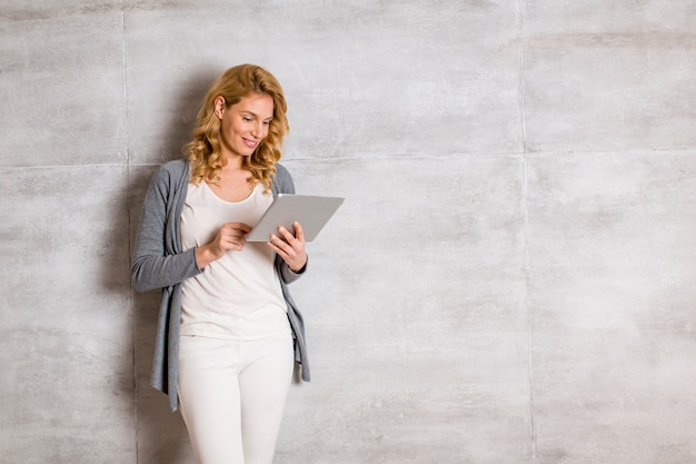 Mujer joven con tableta junto a la pared