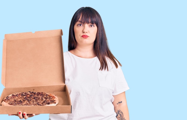 Mujer joven de talla grande con actitud de pensamiento de caja de pizza de entrega y expresión sobria que parece segura de sí misma