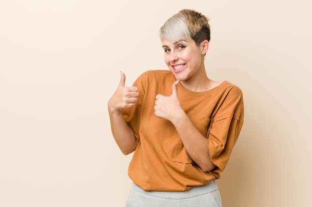 Mujer joven de talla grande con cabello corto levantando ambos pulgares, sonriente y confiado.