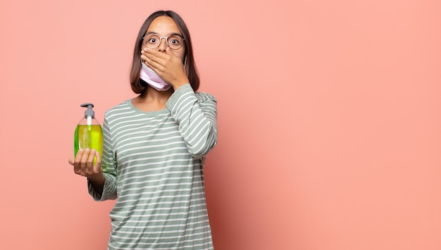 Mujer joven tapándose la boca con las manos con una expresión de sorpresa y sorpresa, manteniendo un secreto o diciendo ¡Ups!