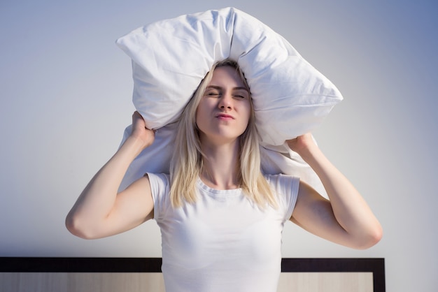 Foto mujer joven tapándose las orejas con una almohada debido al ruido. - imagen