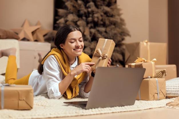 Mujer joven con tarjeta de crédito, compras en línea en un portátil en un acogedor interior navideño