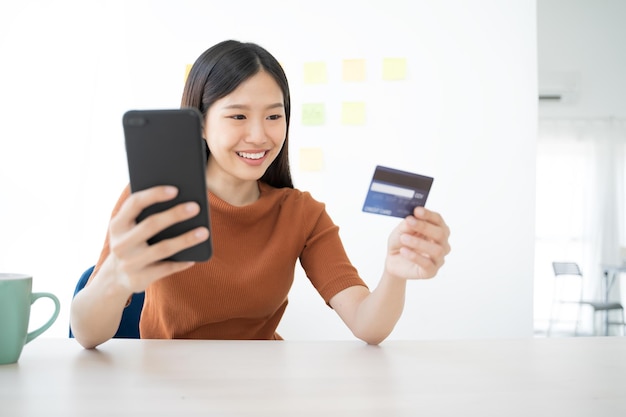 Mujer joven con tarjeta de crédito mientras usa el teléfono móvil para comprar en línea