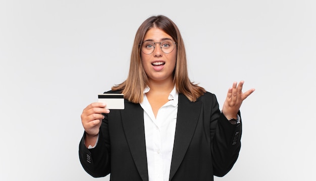 Mujer joven con una tarjeta de crédito que se siente feliz, sorprendida y alegre, sonriendo con actitud positiva, dándose cuenta de una solución o idea