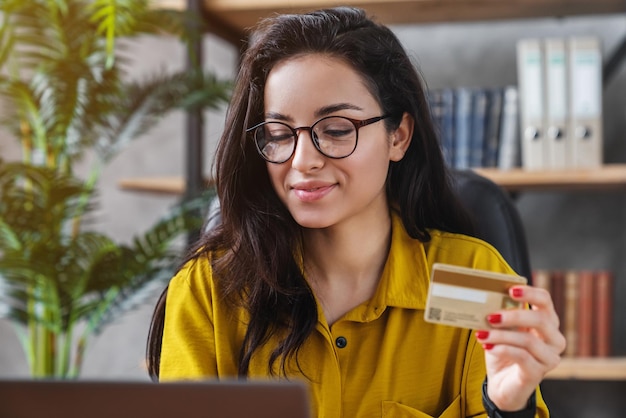 Mujer joven con tarjeta de crédito y usando una computadora portátil en la oficina en casa