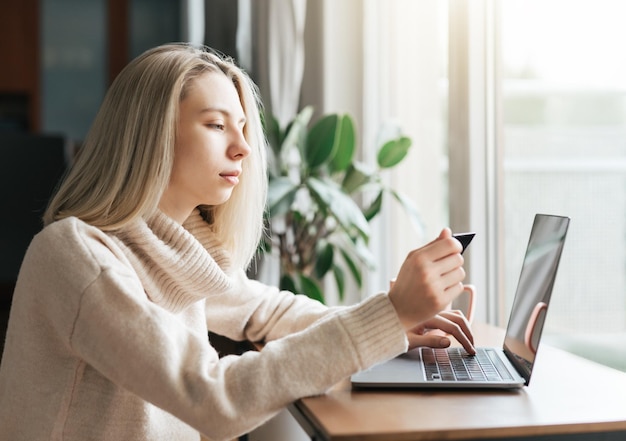 Mujer joven con tarjeta de crédito y usando una computadora portátil