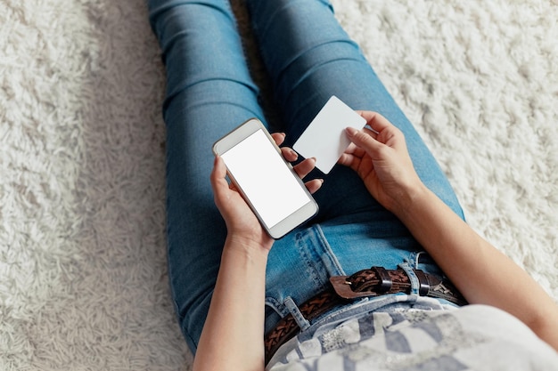 Mujer joven con tarjeta de crédito y usando el teléfono sentado en el piso Pago Concepto de compras en línea