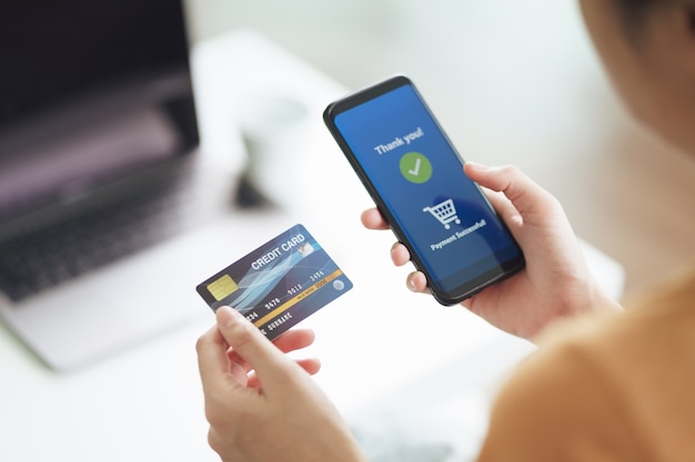 Foto mujer joven con tarjeta de crédito y uso de teléfonos inteligentes para compras en línea, banca por internet, comercio electrónico, gastar dinero, trabajar desde el concepto de hogar.