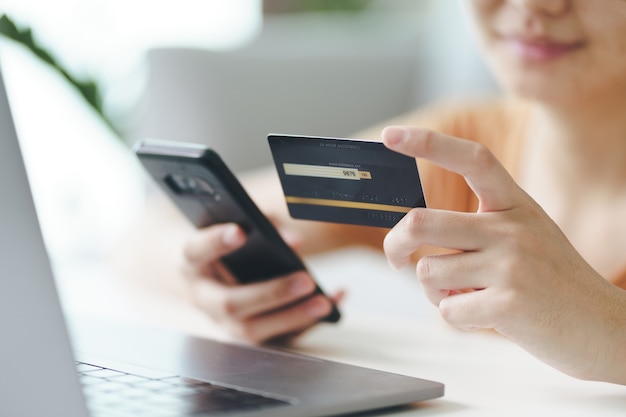 Mujer joven con tarjeta de crédito y uso de teléfonos inteligentes para compras en línea, banca por Internet, comercio electrónico, gastar dinero, trabajar desde el concepto de hogar