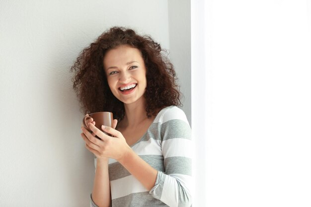 Mujer joven con taza de café aromático en la habitación.