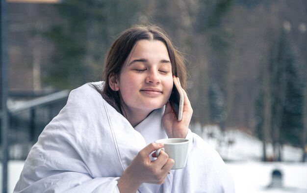 Una mujer joven con una taza de café en el balcón en invierno en las montañas