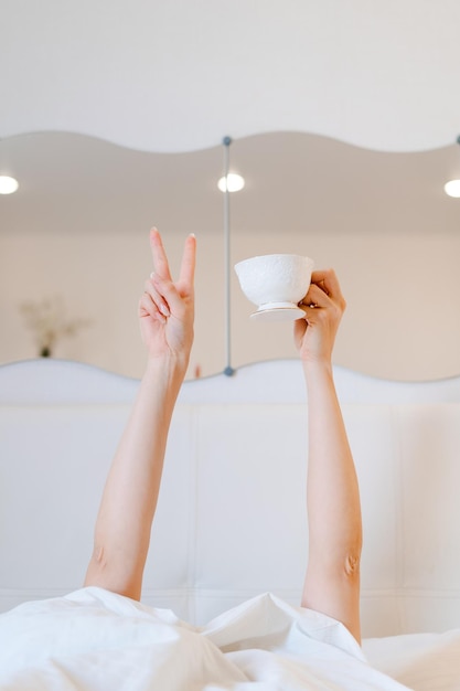 Mujer joven con una taza de café en la cama con sábanas blancas Minimal happy morning